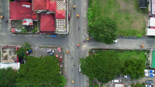 Ascending top-down aerial view of busy intersection in Philippine town district with tricycles and motorcycles driving.