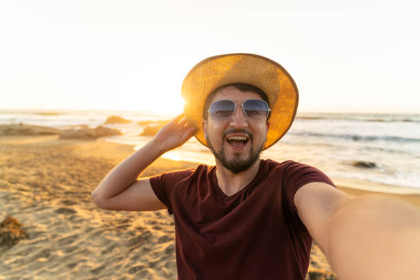 istock Man in stylish sunglasses and a hat snaps a selfie on a beach 2121998484
