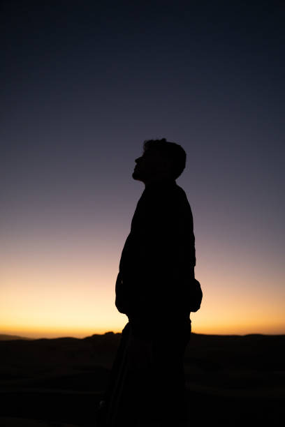 A vertical shot of a silhouetted man against a sunset background