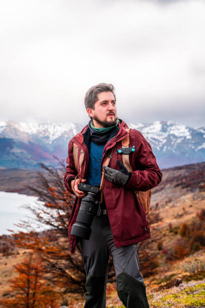 istock Vertical shot of a man with a camera on a mountaintop, surrounded by mountains 2122000046
