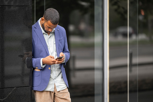 Businessman looking at his smart phone while standing in front of office building in the city.