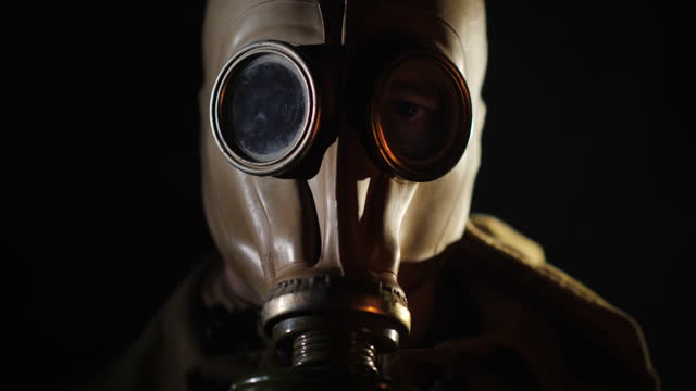 The gleams of the fire are reflected in the eye and gas mask of the man