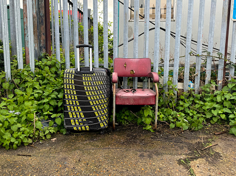 Old seat and suitcase dumped by a fence