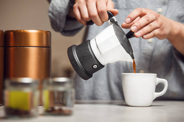 istock Pouring Fresh Coffee From Moka Pot Into White Cup on Kitchen Counter 2122015505