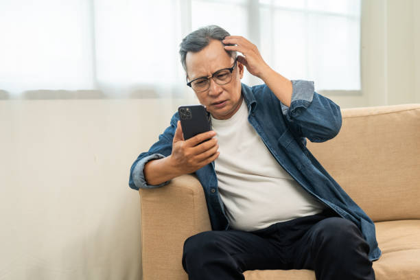 istock Depressed Asian mature old man using smartphone serious thinking on sofa in living room. Portrait stress of senior asian man holding cell phone. Mature People and lifestyle 2122059634