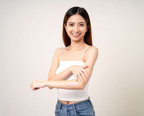 Beautiful smiling happy young asian woman with beauty skin care treatment lotion on the body. Charming female lady standing pose applying body cream Facial treatment beauty and spa