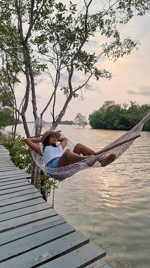 A woman relaxes in a hammock on a dock, enjoying the peaceful waters and gentle breeze on a sunny day. Chantaburi Thailand