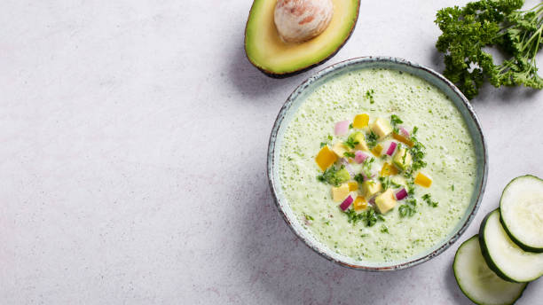 istock Green cucumber gazpacho cold cream soup styled and decorated in rustic bowl with ingredients on gray table, top view 2122102011