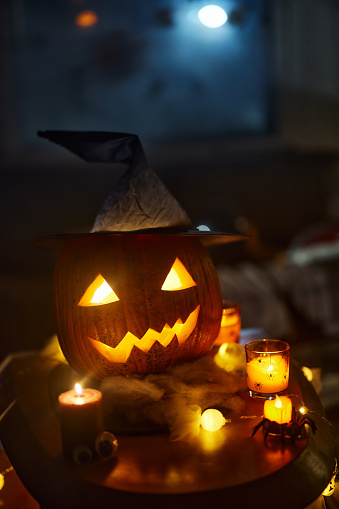 Close up of illuminated carved pumpkin with witch's hat on Halloween.