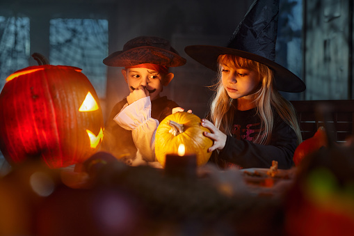 Cute little kids in costumes spending a Halloween with Jack O' Lantern at home.