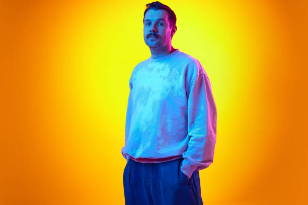 istock Man in his 30s wearing sweatshirt and jeans, standing on gradient yellow orange background in neon light 2122113830