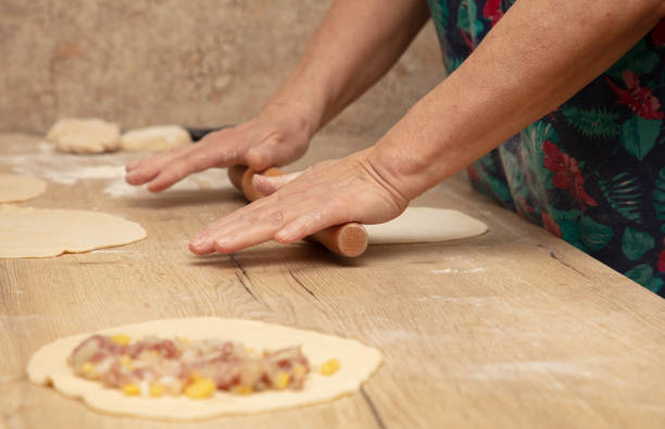 A woman rolls out the dough with a rolling pin on the table.