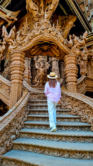 A mysterious woman in a straw hat gracefully descends a staircase with purpose, embodying elegance and adventure. Sanctuary of Truth Pattaya