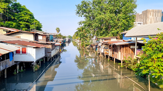 Bangkok Thailand 13 January 2024, A tranquil river winding through lush greenery with quaint houses perched along its banks, creating a picturesque scene of riverside living in harmony with nature.