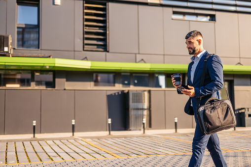 Handsome mid-adult man using his smart phone while drinking coffee in front of an office building.