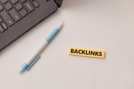 Black laptop, blue pen, yellow sticker has text Backlinks  on the white desk. Concept improve website visibility and rankings on search engines