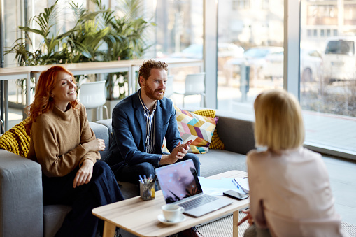 Happy couple communicating with their real estate agent during a meeting at casual office. Focus is on man.