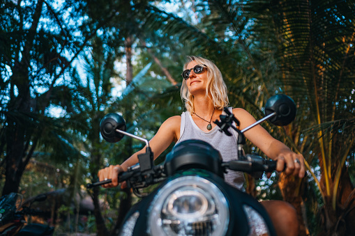 A mid adult woman on a motorcycle. She is enjoying the day, traveling through the beautiful nature on the Ko Phangan island, Thailand.