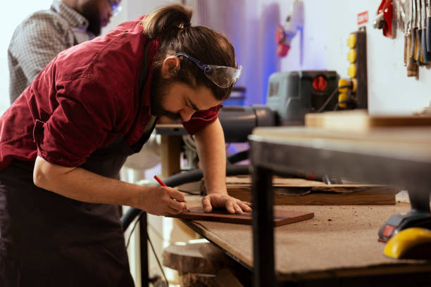 istock Craftsperson using ruler on wood plank with coworker in background 2122188227