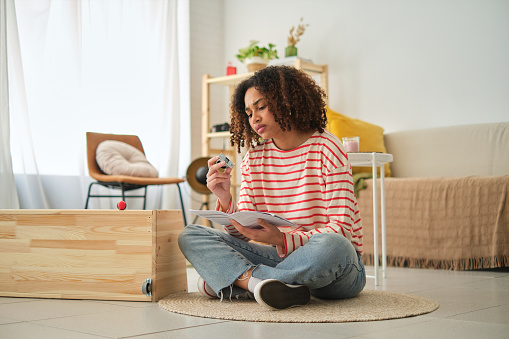 Horizontal photo with copy space of a young african woman reading instructions to assembly furniture at home