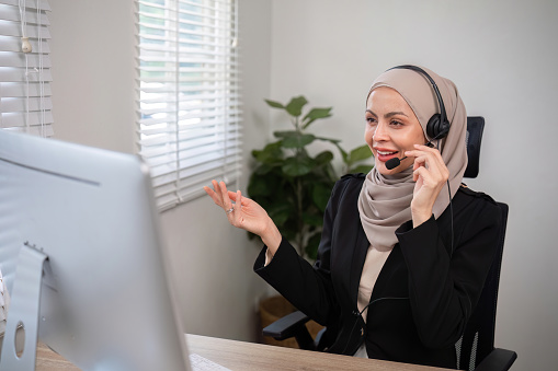 Muslim female call center employee wearing hijab Talking with customers on laptop in customer service office.
