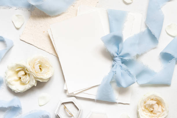 白いテーブルの上面図にクリーム色のバラの近くに水色のリボンで結ばれたカード、結婚式のモックアップ