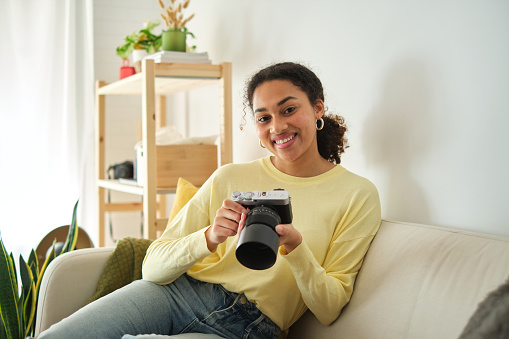 Young african female photographer smiling at camera sitting at home