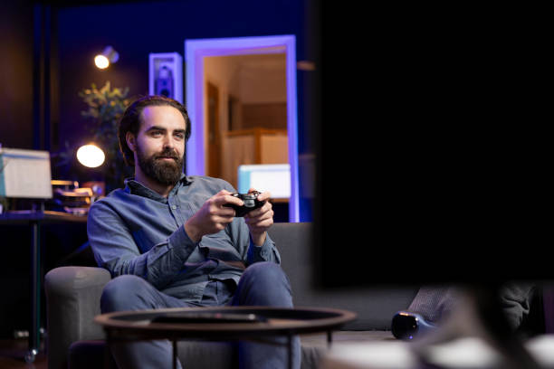 istock Smiling gamer using gamepad to destroy enemies, relaxing at home on couch 2122244800