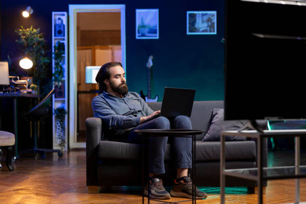 istock Teleworking employee on couch watching TV and working on notebook 2122251088