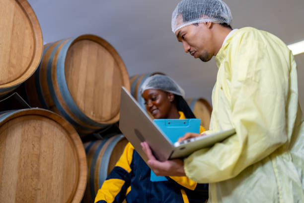 nel cuore di una barricaia, un enologo e un assistente con un computer portatile scrutano il processo di invecchiamento del vino, garantendo la perfezione dell'annata. - wine wine rack winery black foto e immagini stock