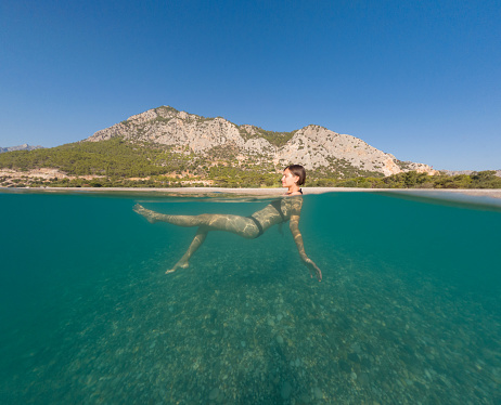 Young female on holidays enjoy floating on a crystal clear water beach of Antalya Turkey. Asian beautiful woman swimming with open arms. Relax and tranquility. Travel and Holiday concept.