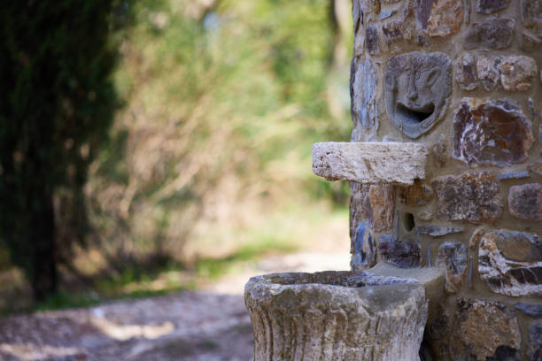 Close-up of old fountain with gargoyle carving on textured stone retaining wall at Chiusdino