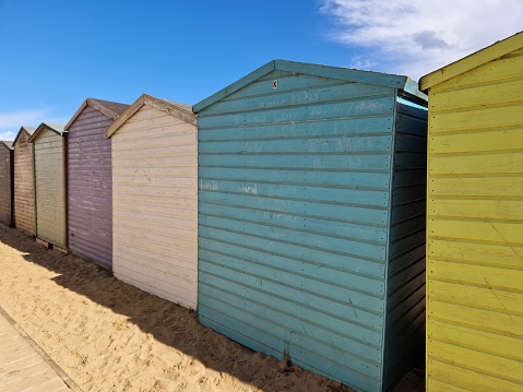 Row of bright, colorful beach huts on sandy beach on the Kentish coast against a blue sky