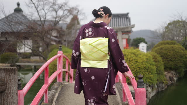 Rear view of Japanese woman in kimono walking across the shrine bridge - slow motion
