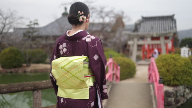 Rear view of Japanese woman in kimono walking across the shrine bridge - part 1 of 2