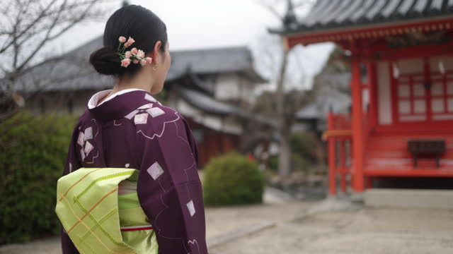 Rear view of Japanese woman in kimono walking across the shrine bridge - slow motion