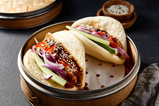 istock Authentic Asian cuisine: Bao buns with duck and vegetables in a steamer on a black table 2122346200