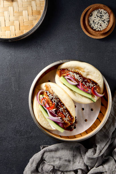 istock Steamed Bao buns with crispy duck, vegetables, and sesame seeds, top view on a dark table 2122346203