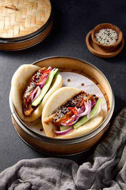 istock Authentic Asian cuisine: Bao buns with duck and vegetables in a steamer on a black table 2122346206