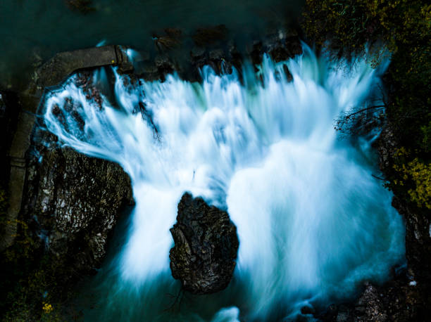 A massive waterfall cascades down rocky terrain near boulders.