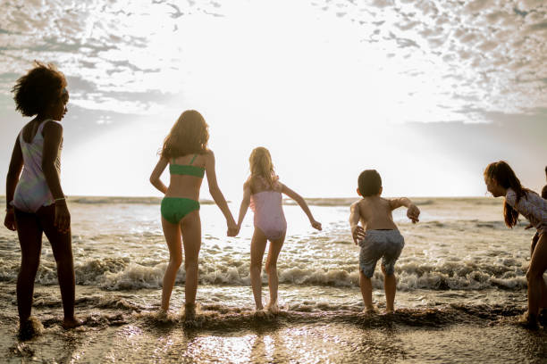 Friend children playing jumping in the waves on beach