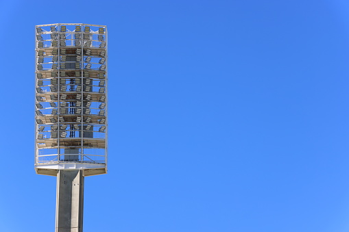 Light-emitting diode (LED) light tower, or floodlights, at large sports stadium or venue.  Clear blue sky background.  Copy space to right.