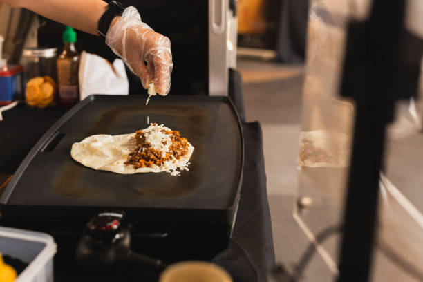 istock Chef sprinkles a tortilla with cheese preparing fresh quesadilla on black grill. 2122418007