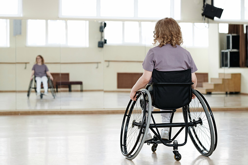 Selective focus rear view shot of unrecognizable young woman with disability in wheelchair practicing dance