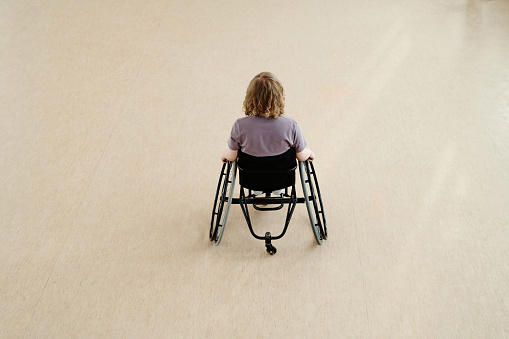 High angle view of unrecognizable young woman in wheelchair dancing alone in spacious studio