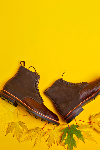 Premium Dark Brown Grain Brogue Derby Boots Made of Calf Leather with Rubber Sole Placed With Maple Leaves Over Yellow. Vertical Image