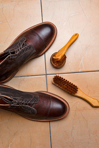 Cleaning Accessories for Dark Brown Grain Brogue Derby Boots Made of Calf Leather Over Tile Background with Special Tools. Vertical image