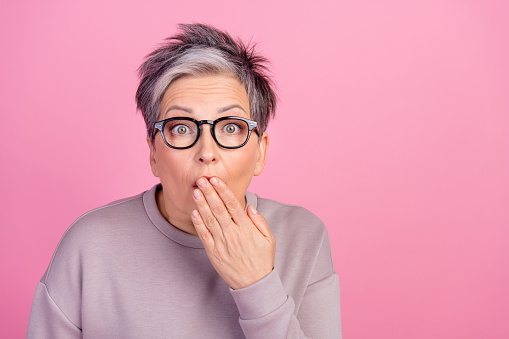 Closeup portrait photo of mature age dyed short grey haircut businesswoman close hand mouth oops isolated on pink color background.