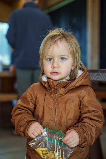 Two year old Eurasian boy wearing a winter jacket and eating crackers while looking directly at the camera.
