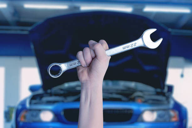 istock Wrench in hand in front of a blue car with an open engine compartment. Ready for service and maintenance. Professional automotive concept 2122479992